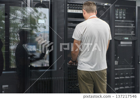 Data center technician working on server racks in a secure IT room performing maintenance and troubleshooting Data center technician working on server racks in a secure IT room performing maintenance and troubleshooting 137217546
