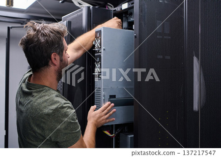It technician performing server maintenance in a data center rack handling hardware installation and repair It technician performing server maintenance in a data center rack handling hardware installation and repair 137217547