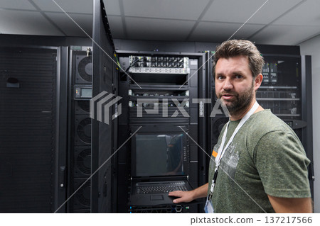 IT technician working in a data center with server racks and network equipment IT technician working in a data center with server racks and network equipment 137217566