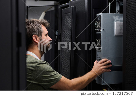 Data center technician performing server maintenance in a rack-filled server room 137217567