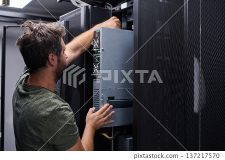 IT technician installing server hardware in a data center server rack performing maintenance and network setup IT technician installing server hardware in a data center server rack performing maintenance and network setup 137217570