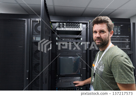 IT technician working in a data center server room checking rack equipment and network systems 137217573