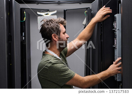 IT technician working on server rack in a data center performing hardware maintenance and installation IT technician working on server rack in a data center performing hardware maintenance and installation 137217583