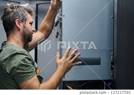 Data center technician installing a server module in a network rack during hardware maintenance Data center technician installing a server module in a network rack during hardware maintenance 137217591