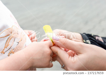 Child healthcare routine. Toddler finger bandaged by mother hands. Daily care concept. 137217659