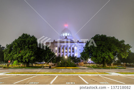 Scenic night view of the illuminated classical facade and dome of the Oklahoma State Capitol building from an empty parking lot on a foggy night in Oklahoma City, Oklahoma, United States. Scenic night view of the illuminated classical facade and dome of the Oklahoma State Capitol building from an empty parking lot on a foggy night in Oklahoma City, Oklahoma, United States. 137218082