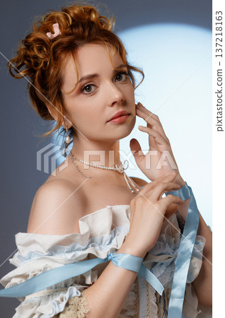 Young woman in ornate Rococo dress holding blue rope near her face against blue background 137218163