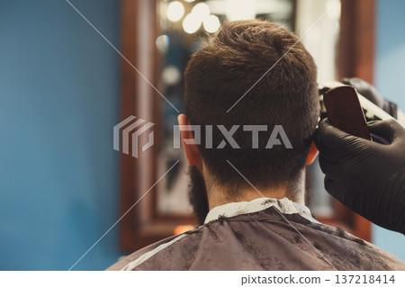 Barber make haircut with hair clipper in barbershop, closeup of client's head. Stylish hairdresser in male hair salon, copy space 137218414