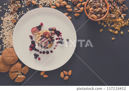 Healthy eating, dieting and detox concept - wholegrain fresh oatmeal porridge on plate with fruits, berries, cookies and nuts on dark background. Still life, top view. 137218452