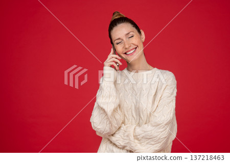 Young woman on red background speaking on the phone and looking pleased Young woman on red background speaking on the phone and looking pleased 137218463