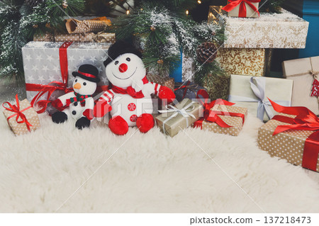Cozy winter holidays background. Funny toy snowmen and presents waiting for christmas under decorated fir tree. Joyful and magical atmosphere of new year eve, copy space Cozy winter holidays background. Funny toy snowmen and presents waiting for christmas under decorated fir tree. Joyful and magical atmosphere of new year eve, copy space 137218473