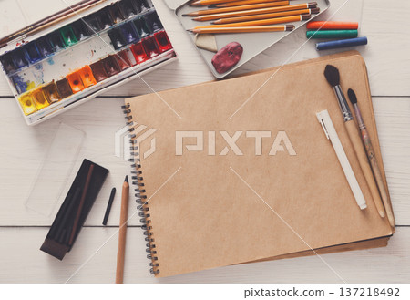 Artist working space background. Watercolor paints and blank craft paper on white wooden desk, top view, flat lay, copy space Artist working space background. Watercolor paints and blank craft paper on white wooden desk, top view, flat lay, copy space 137218492