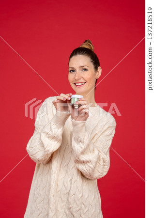 Beautiful young woman on red background with a jar of cream in hand 137218519