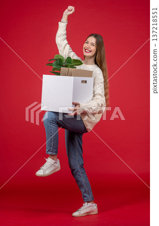 Pretty smiling young woman with a box with a home plant in it Pretty smiling young woman with a box with a home plant in it 137218551