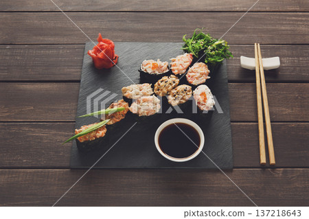 Japanese food restaurant, sushi gunkan roll plate, platter set. Creative food. Set with chopsticks, ginger, soy, wasabi. Sushi at rustic wood background and black stone. POV, horizontal image 137218643