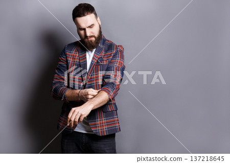 Bearded man in checkered jacket preparing to work hard, adjusting sleeves, copy space, gray studio background 137218645