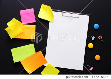 Sticky notes in bright colors surround a blank clipboard on a black surface. The assortment adds a lively touch to a workspace, inviting creativity and organization. Sticky notes in bright colors surround a blank clipboard on a black surface. The assortment adds a lively touch to a workspace, inviting creativity and organization. 137218666
