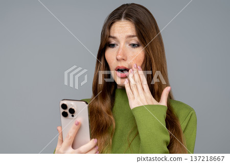Young woman reading a message on her phone and looking shocked Young woman reading a message on her phone and looking shocked 137218667