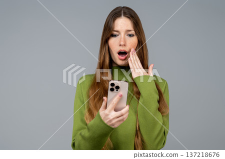 Young woman reading a message on her phone and looking shocked Young woman reading a message on her phone and looking shocked 137218676