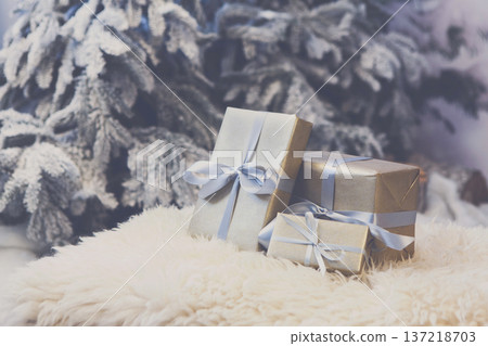 Christmas gifts decorated with silver satin ribbon bows on soft fluffy carpet at blurred snowy fir tree background, closeup, selective focus. Winter holidays concept 137218703