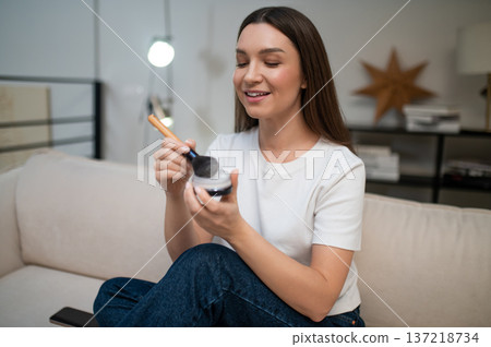 Young woman sitting on the sofa and doing make up Young woman sitting on the sofa and doing make up 137218734