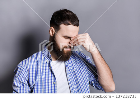 Depressed bearded man with closed eyes touching his face. Young guy feeling hopeless, having headache, gray studio background. Depressed bearded man with closed eyes touching his face. Young guy feeling hopeless, having headache, gray studio background. 137218735