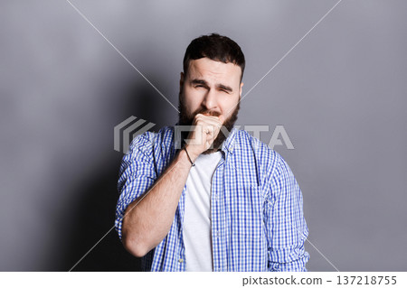 Portrait of yawning bearded man. Sleepy guy gape and close his mouth with hand, gray studio background Portrait of yawning bearded man. Sleepy guy gape and close his mouth with hand, gray studio background 137218755