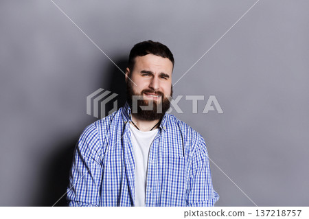 Bearded man expressing disgust on face, grimacing on camera, gray studio background. Negative emotions 137218757