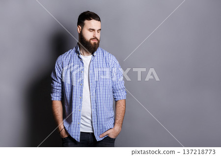Handsome bearded man posing with hands in pocket. Portrait of young confident guy looking away, gray studio background, copy space Handsome bearded man posing with hands in pocket. Portrait of young confident guy looking away, gray studio background, copy space 137218773