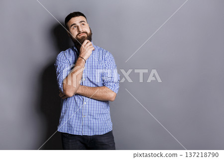 Pensive young bearded man looking upwards. Handsome relaxed guy dreaming about something, lost in thoughts, gray studio background Pensive young bearded man looking upwards. Handsome relaxed guy dreaming about something, lost in thoughts, gray studio background 137218790