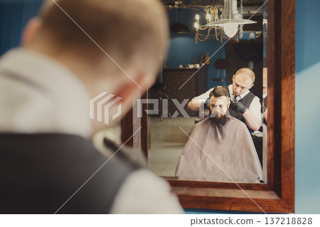 Man getting haircut by hairstylist at barbershop. Stylish barber and client in mirror Man getting haircut by hairstylist at barbershop. Stylish barber and client in mirror 137218828