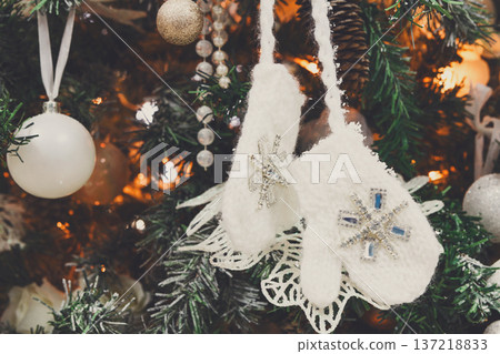 Winter holidays atmosphere background. Closeup of beautifully decorated fir tree with modern shiny baubles, beards, garland and small knitted mittens . Christmas and new year magic at home 137218833