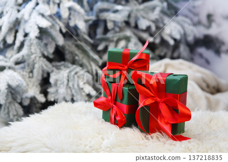 Christmas gifts decorated with red ribbon bows on soft fluffy carpet at blurred snowy fir tree background, closeup, selective focus. Winter holidays concept 137218835