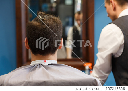 Man look at haircut by hairstylist at barbershop, closeup of client's head. Stylish barber and client in mirror 137218838