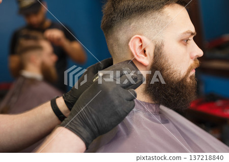 Barber styling beard with trimmer at barbershop, closeup of client's head. Barbershop for men 137218840