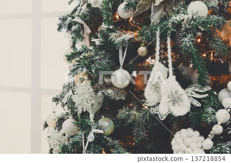 Winter holidays atmosphere background. Closeup of beautifully decorated fir tree with modern shiny baubles, beards, garland and small knitted mittens . Christmas and new year magic at home, copy space Winter holidays atmosphere background. Closeup of beautifully decorated fir tree with modern shiny baubles, beards, garland and small knitted mittens . Christmas and new year magic at home, copy space 137218854