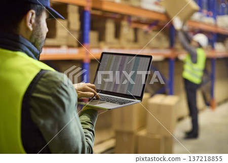 Warehouse inventory with worker using laptop to track stock on shelving racks 137218855