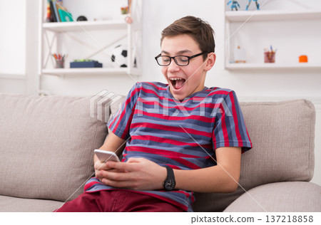 Teenager playing games on smartphone. Winner in online competition, sitting on comfortable couch at home 137218858