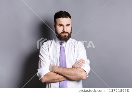 Confident businessman with serious face and crossed hands. Successful man in white shirt with purple tie looking at camera, gray studio background Confident businessman with serious face and crossed hands. Successful man in white shirt with purple tie looking at camera, gray studio background 137218958
