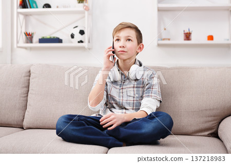 Teenager talking on mobile. Phone call distracted boy from listening to music at home. Stylish kid in checkered shirt and jeans with headphones on the neck chatting with friend Teenager talking on mobile. Phone call distracted boy from listening to music at home. Stylish kid in checkered shirt and jeans with headphones on the neck chatting with friend 137218983