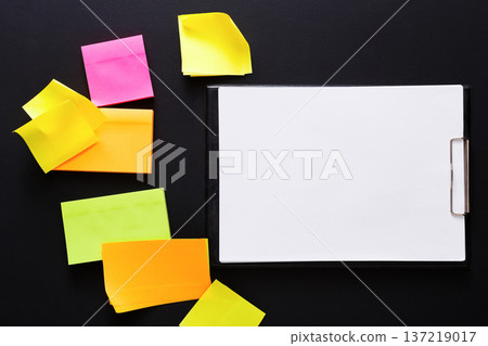 A cluttered workspace features vibrant sticky notes in various colors scattered around a blank clipboard. The clipboard awaits ideas or tasks, encouraging creativity and organization. A cluttered workspace features vibrant sticky notes in various colors scattered around a blank clipboard. The clipboard awaits ideas or tasks, encouraging creativity and organization. 137219017