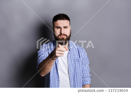 Strict serious young bearded man point with index finger on camera, gray studio background. Motivation poster Strict serious young bearded man point with index finger on camera, gray studio background. Motivation poster 137219034
