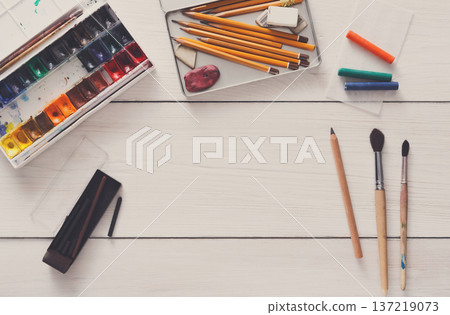 Drawing tools, stationary supplies, workplace of artist. Watercolor paints and blank paper on white wooden desk, top view, flat lay, copy space 137219073