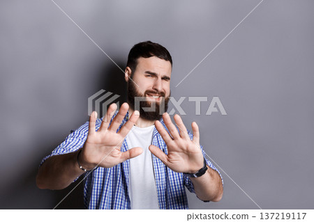 Bearded pushing away with his hands in foreground, expressing his refusal, aversion or repulsion with stopping hand gesture, gray studio background Bearded pushing away with his hands in foreground, expressing his refusal, aversion or repulsion with stopping hand gesture, gray studio background 137219117