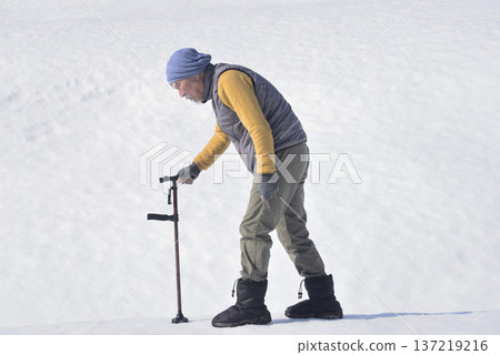 An elderly man doing rehabilitation using a walking stick on the snow 137219216