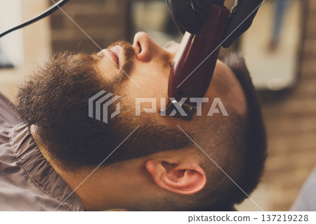 Barber styling beard with trimmer at barbershop, closeup. Barbershop for men Barber styling beard with trimmer at barbershop, closeup. Barbershop for men 137219228