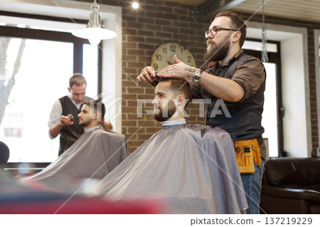 Barbers make haircut to clients at barbershop. Stylish hairdressers in male hair salon 137219229