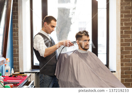 Barber make beard haircut with trimmer hair clipper in barbershop. Hairstyle in barbershop. Barber make beard haircut with trimmer hair clipper in barbershop. Hairstyle in barbershop. 137219233