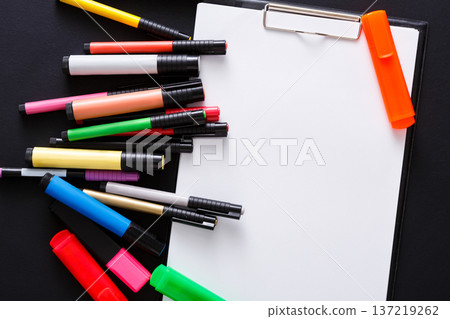 A variety of colorful markers are scattered around a blank notepad on a black surface. The setup invites creativity and artistic exploration, perfect for drawing or writing. A variety of colorful markers are scattered around a blank notepad on a black surface. The setup invites creativity and artistic exploration, perfect for drawing or writing. 137219262