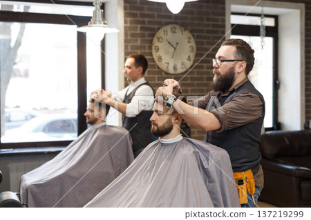 Barber make haircut with scissors at barbershop. Stylish hairdresser in male hair salon 137219299